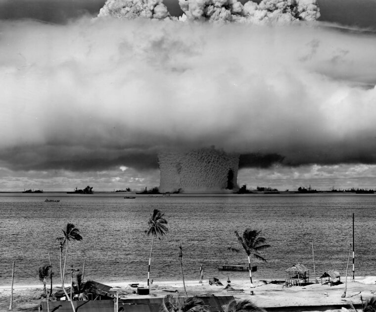 A black and white image of a mushroom cloud, seen from a tropical beach