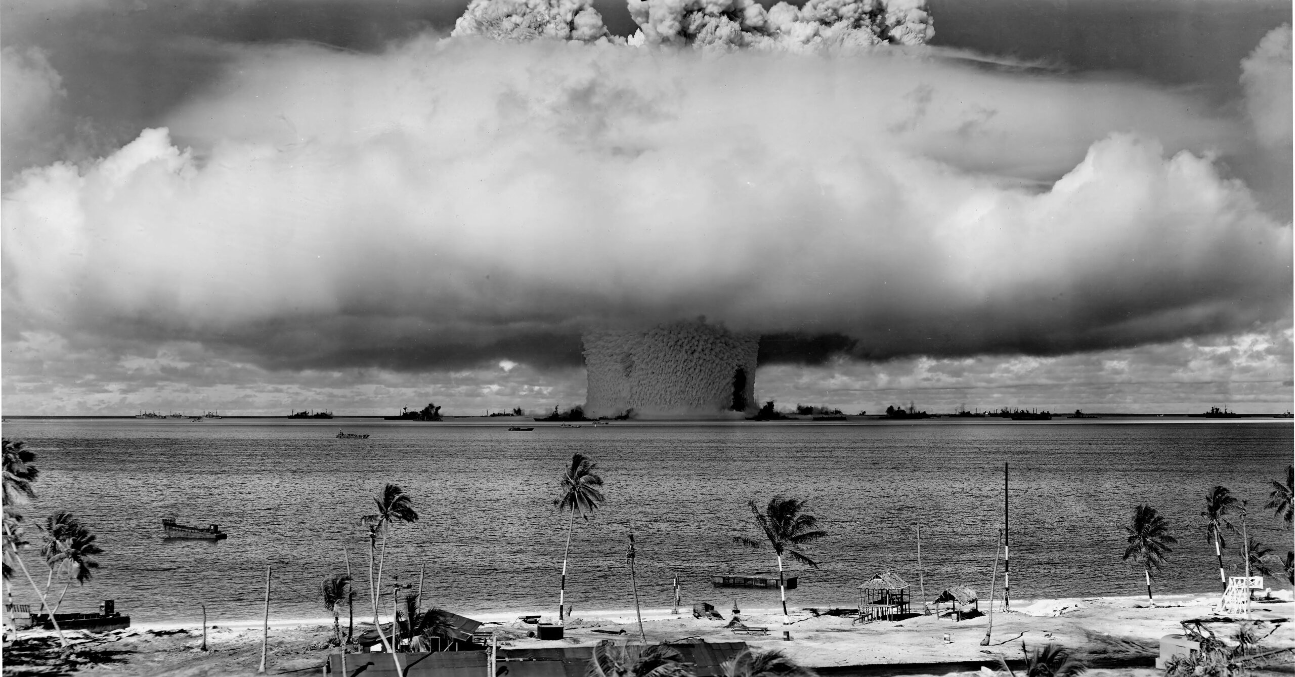 A black and white image of a mushroom cloud, seen from a tropical beach